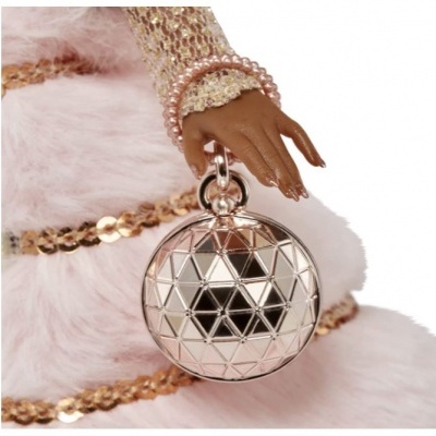 Mão segurando bolsa redonda prateada com padrão geométrico, fundo tecido peludo rosa claro