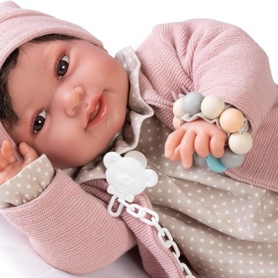 Boneca de bebé com roupa rosa e bege, segurando chocalho colorido e chupeta branca
