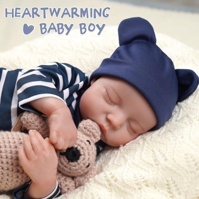 Boneco bebé a dormir com pijama azul às riscas e gorro azul, segurando ursinho de croché sobre manta branca