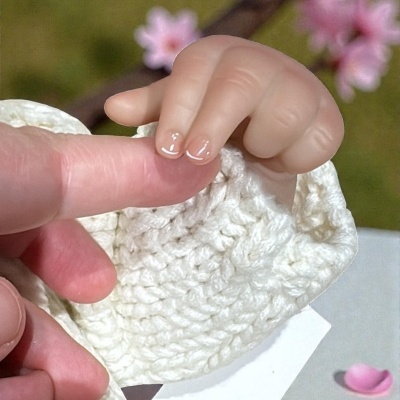 Mão de bebé segura dedo de adulto com pano branco e pétalas cor-de-rosa ao fundo