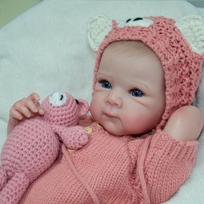 Boneca bebé vestida com roupa de malha rosa e gorro com orelhas brancas segurando boneco tecido rosa