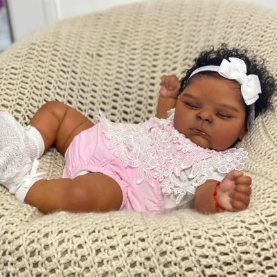 Boneca realista de bebé vestida de rosa e branco deitada numa almofada creme