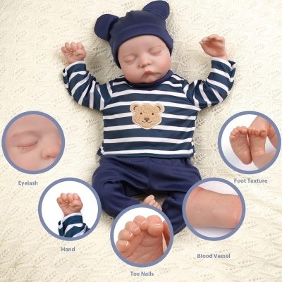Boneco bebé realista com roupa azul e branca com padrão de urso, sobre tecido branco com detalhes de partes do corpo em círculos