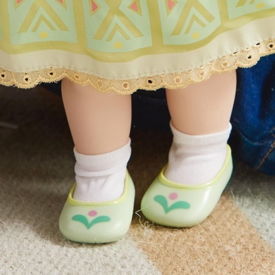 Pernas de boneca com meias brancas e sapatos verdes de padrão floral com saia verde com renda na barra