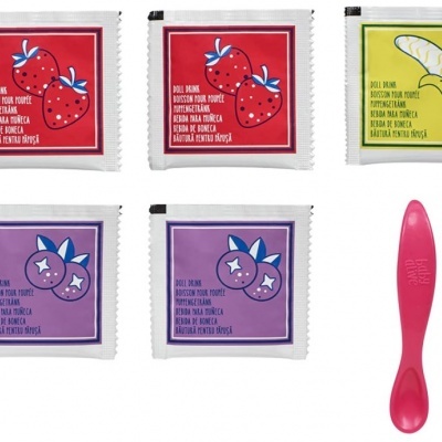 Pacotes de purê de frutas com colher rosa ao lado.