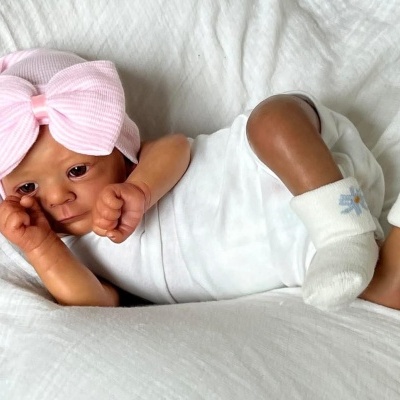 Boneca realista de bebé com touca rosa e body branco deitada