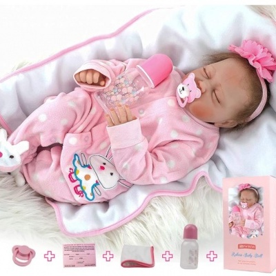 Boneca bebê reborn em fato de pijama rosa deitada em cobertor branco rosa segurando mamadeira
