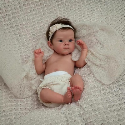 Boneca reborn realista vestida com faixa de cabeça branca com flor e fralda creme, sobre manta de malha creme