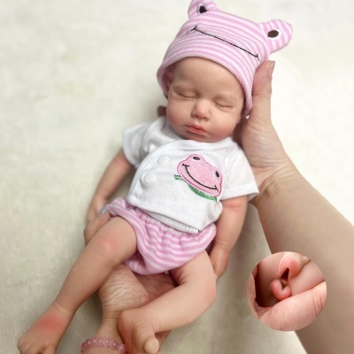 Boneca realista com roupinha branca e rosa e gorro rosa às riscas segurada por mãos.