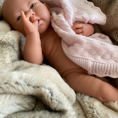Boneca bebé realista com manta rosa clara num fundo peludo bege