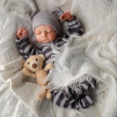 Bebé adormecido com pijama listrado e chapéu cinzento com orelhas, coberto com manta branca, segurando urso de peluche.