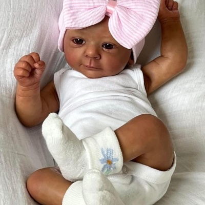 Boneca bebé realista com roupa branca e gorro rosa com laço