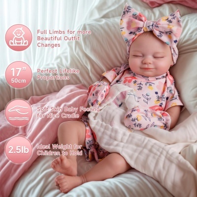 Boneca realista vestida com macacão e laço rosa com padrão floral deitada num berço com roupa branca e rosa