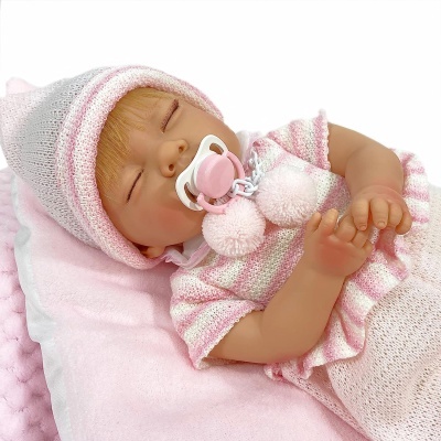 Bebé reborn vestido de malha rosa e branco com chupeta rosa deitado numa almofada rosa