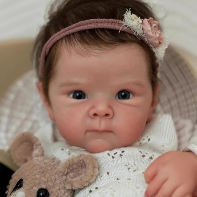 Boneca de bebé realista com vestido branco e ursinho de peluche castanho