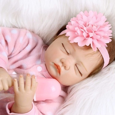 Boneca bebé realista com pijama rosa a segurar mamadeira rosa num fundo branco macio