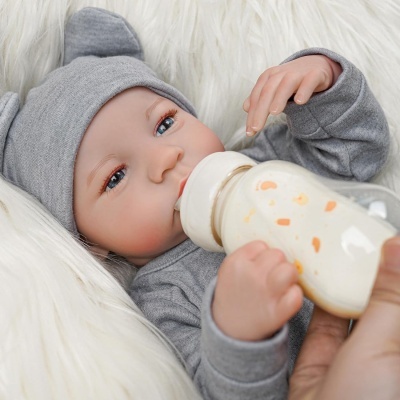 Boneca bebé realista com roupa cinza e biberão branco a ser alimentada