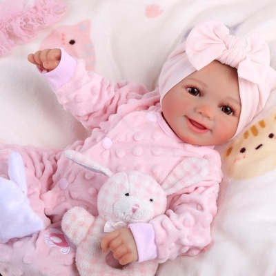 Boneca bebé realista com pijama rosa e faixa de cabelo com laço, deitada com coelho de peluche