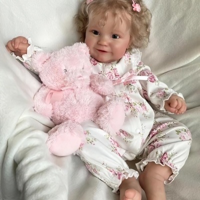 Boneca realista com macacão floral e ursinho de peluche cor-de-rosa