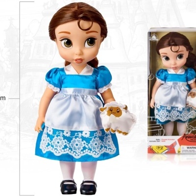Boneca vestida de azul com avental branco segurando ovelha de pelúcia ao lado da sua embalagem