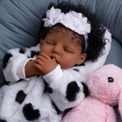 Boneca bebé realista com casaco branco e manchas pretas e peluche rosa