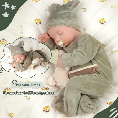 Boneca realista a dormir vestida com fato verde oliva com capuz e orelhas, chupeta e brinquedo suave num fundo branco com padrão de ursinhos