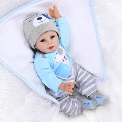 Boneca bebé com roupa azul e cinza deitada numa manta branca