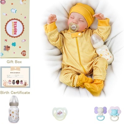 Boneca reborn vestida de amarelo com chucha e biberão ao lado da embalagem e acessórios.