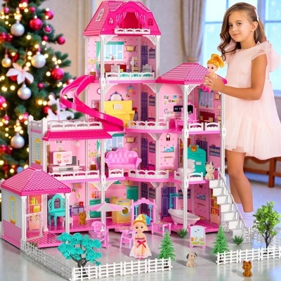 Casa de bonecas rosa e branca com móveis e bonecas, mãos de menina loira a brincar, árvore de Natal ao fundo.