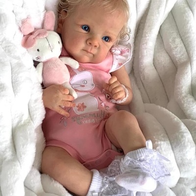 Boneca bebé realista com roupa cor-de-rosa e peluche sobre manta branca