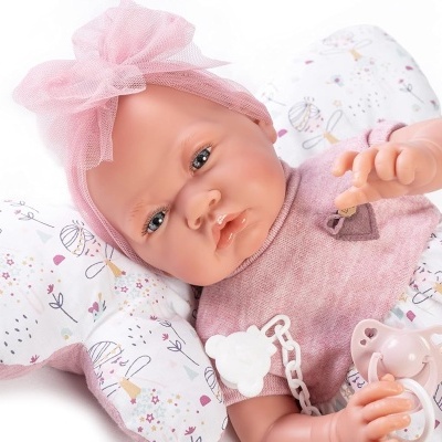 Boneca bebé com roupa e faixa cor-de-rosa sobre almofada branca com padrões coloridos