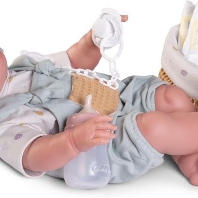 Boneca bebé realista com roupa azul e branca e biberão ao lado de um cesto com fraldas