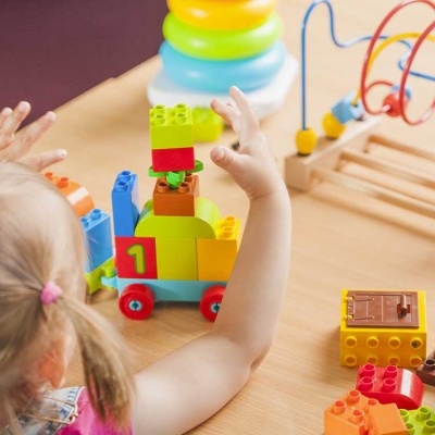 Criança loira a brincar com blocos de construção coloridos de plástico sobre mesa de madeira clara