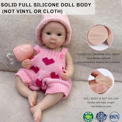 Boneca de silicone com macacão rosa e gorro sentada sobre superfície bege.