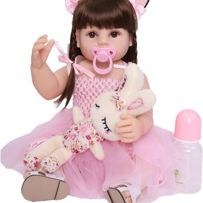 Boneca infantil vestida de rosa a segurar um coelho de pelúcia e uma chupeta rosa com um biberão ao lado