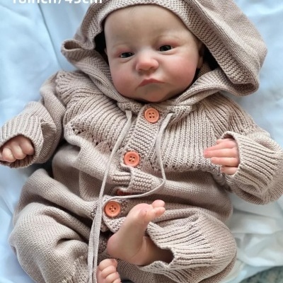 Boneca bebé realista com fato de malha bege e capuz de botão laranja deitada