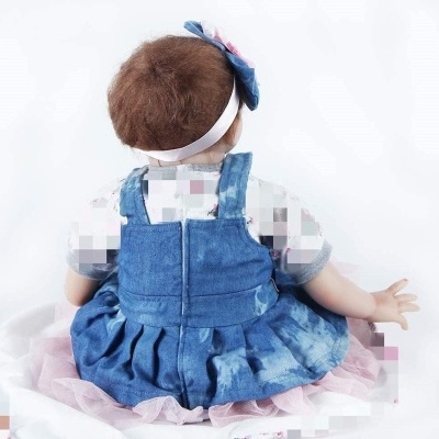 Boneca bebé vestida com vestido azul de ganga e fita de cabelo, sentada de costas