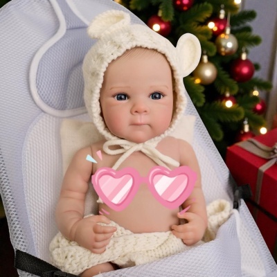 Boneca bebé realista com gorro de malha creme com orelhas e árvore de Natal ao fundo