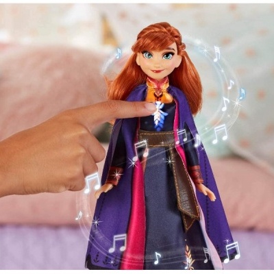 Boneca vestida com capa roxa e vestido azul e rosa com mão infantil interagindo.