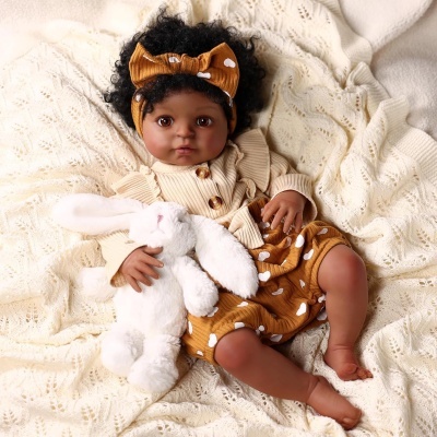 Boneca bebé negra com roupa castanha e creme deitada com coelho de peluche branco