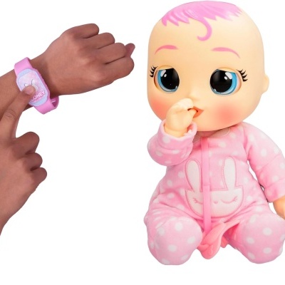 Boneca bebé cor-de-rosa sentada ao lado de mão a usar pulseira cor-de-rosa