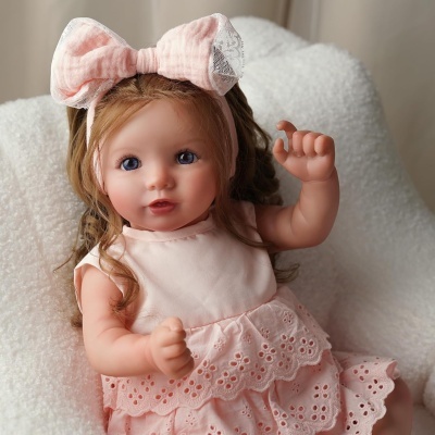 Boneca bebé com vestido rosa e laço na cabeça sentada numa cadeira branca