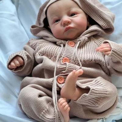 Bebé com fato de malha bege com capuz e botões laranja deitado