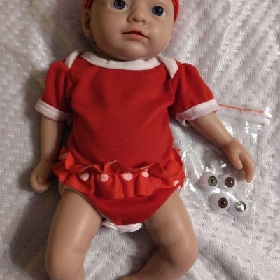 Boneca de bebé com roupa vermelha e chapéu de bolinhas em tecido branco