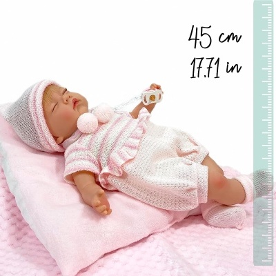 Boneca bebé vestida de malha branca e rosa deitada numa almofada cor de rosa com régua ao lado