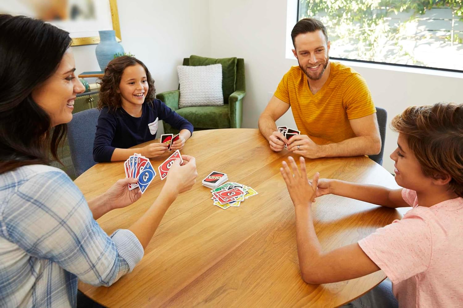 JOGO DE CARTAS UNO CLÁSSICO, MATTEL Cartas UNO coloridas num jogo de cartas em família à volta de mesa de madeira
