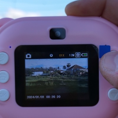 Câmara digital rosa com ecrã mostrando paisagem rural e data 2024/01/01.