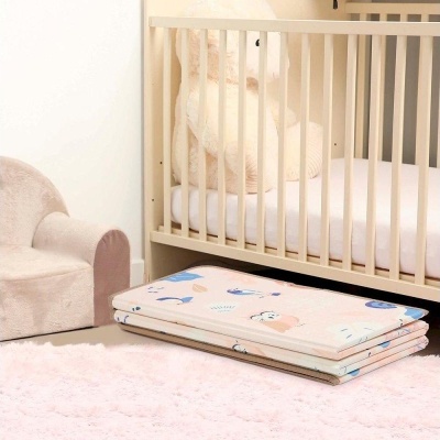Tapete dobrável colorido para crianças ao pé de berço branco e cadeira rosa