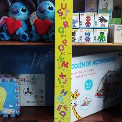 Medidor infantil amarelo com letras coloridas e números, em ambiente com brinquedos e peluches