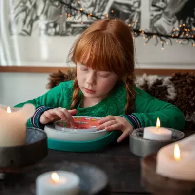 Criança a brincar com brinquedo redondo colorido e velas acesas num ambiente interior acolhedor.